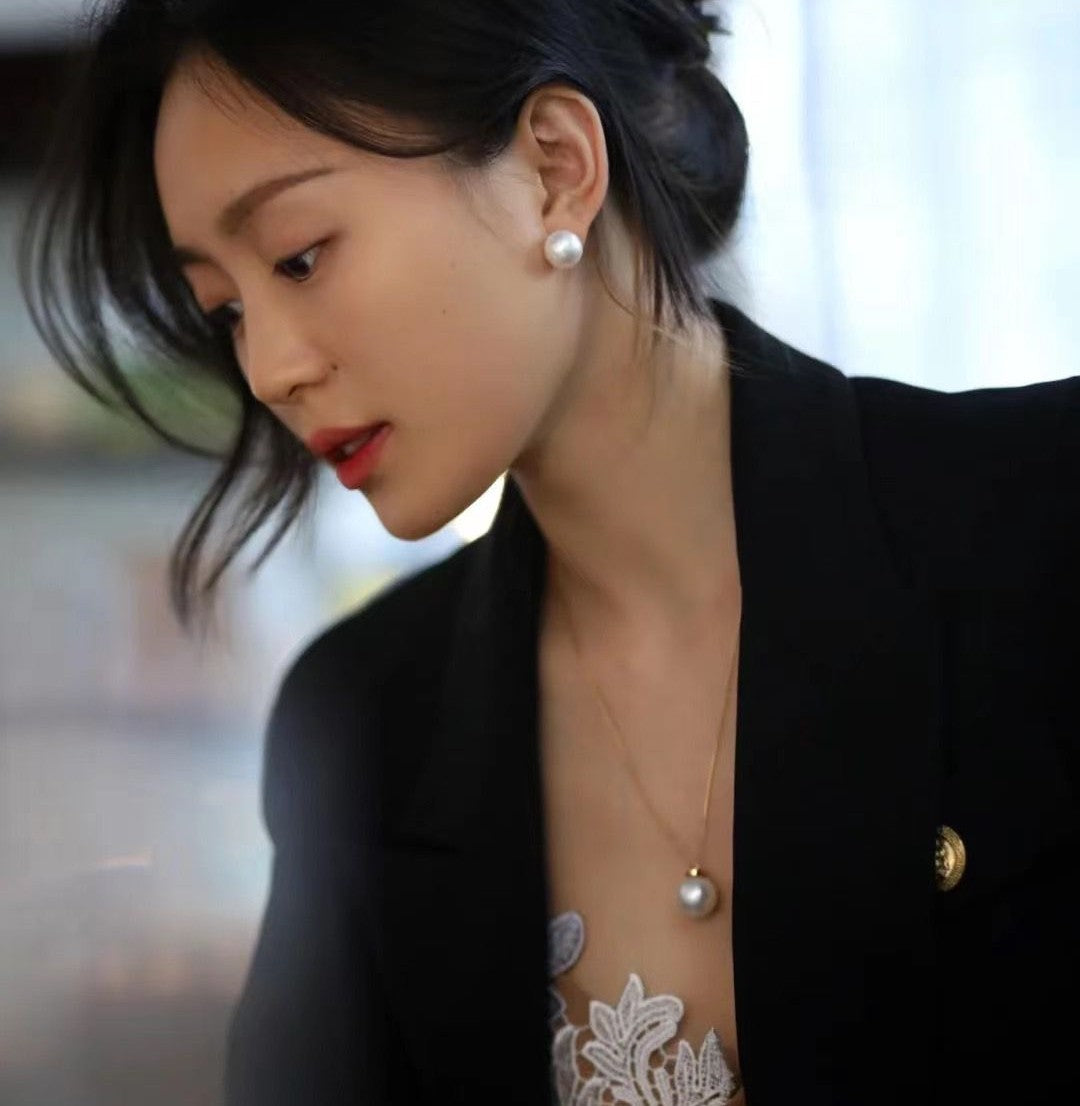 A woman in pearl stud earrings and a pendant from Timeless Pearl, styled with a black blazer and lace top.