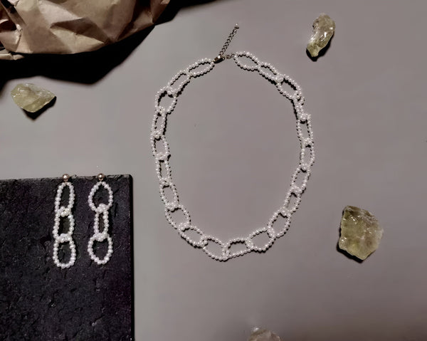  A Timeless Pearl earring pair and necklace placed near gemstones.