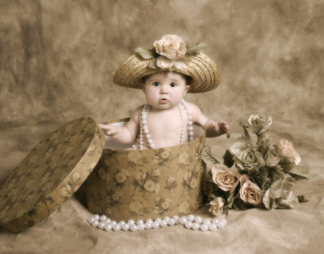 Baby in a straw hat with flowers, sitting in a floral hatbox, draped in pearls from Timeless Pearl.