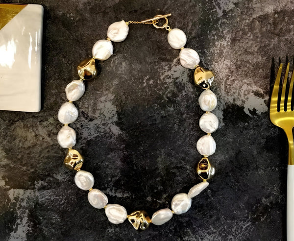 Timeless Pearl’s Baroque pearl necklace with gold, organically-shaped heart beads and a gold toggle clasp on a dark surface.