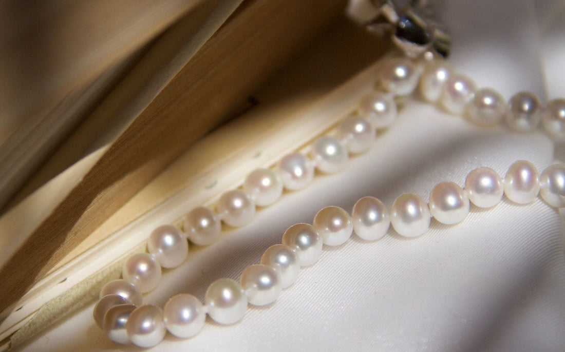 Classic pearl necklace by Timeless Pearl, abreast of a rusted book on white silk cloth.