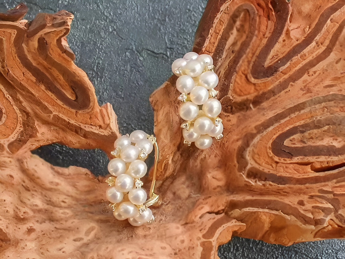 Gold hoop earrings adorned with clusters of white pearls from Timeless Pearl, displayed on textured brown wood.