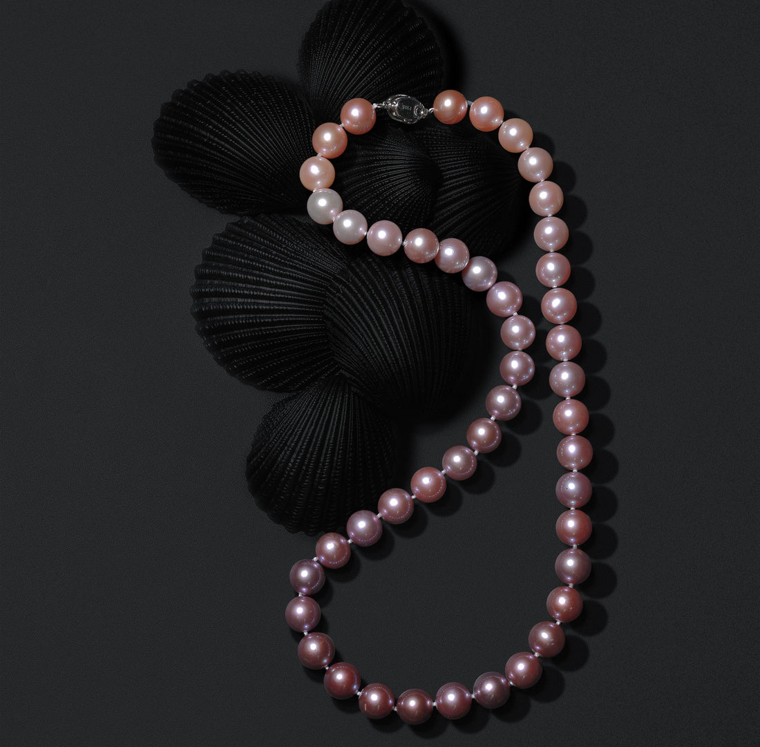 Elegant strand of blush to deep pink pearls from Timeless Pearl, styled on black seashells for a modern, luxurious look.