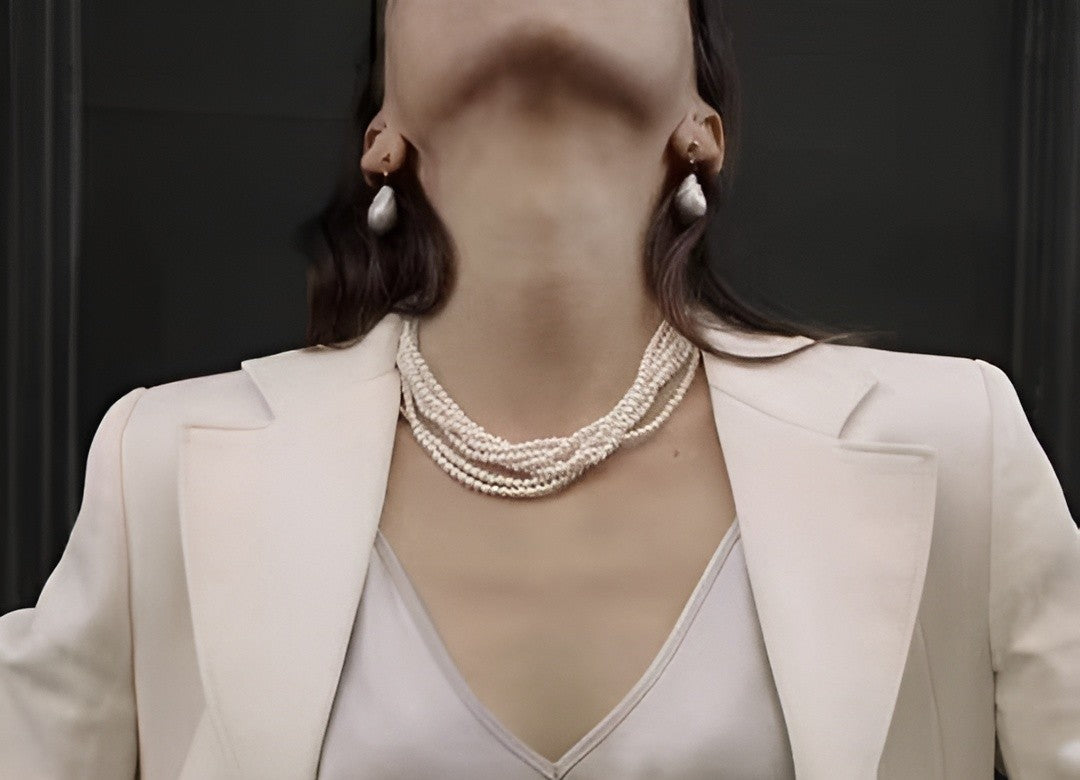Timeless Pearl's elegant multi-strand pearl necklace and baroque earrings grace a chic white blazer ensemble.