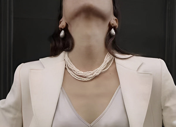 Timeless Pearl's elegant multi-strand pearl necklace and baroque earrings grace a chic white blazer ensemble.