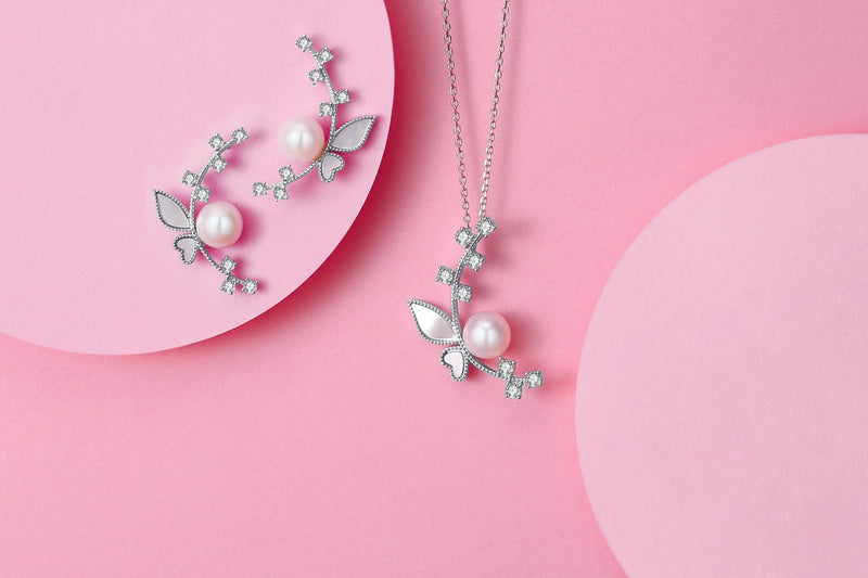 Timeless Pearl floral pearl necklace and earrings with silver leaf details on a pink backdrop.