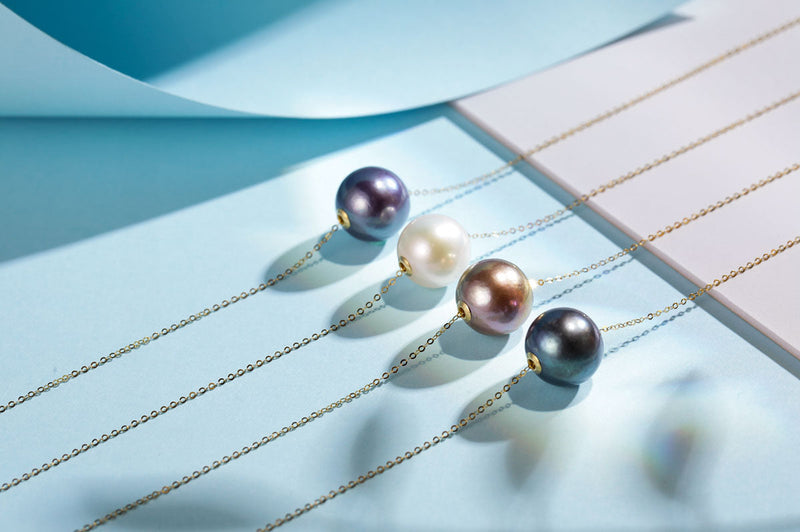 Timeless Pearl necklaces with pearls of different colors tied to gold chains laid out across an aqua-colored surface.