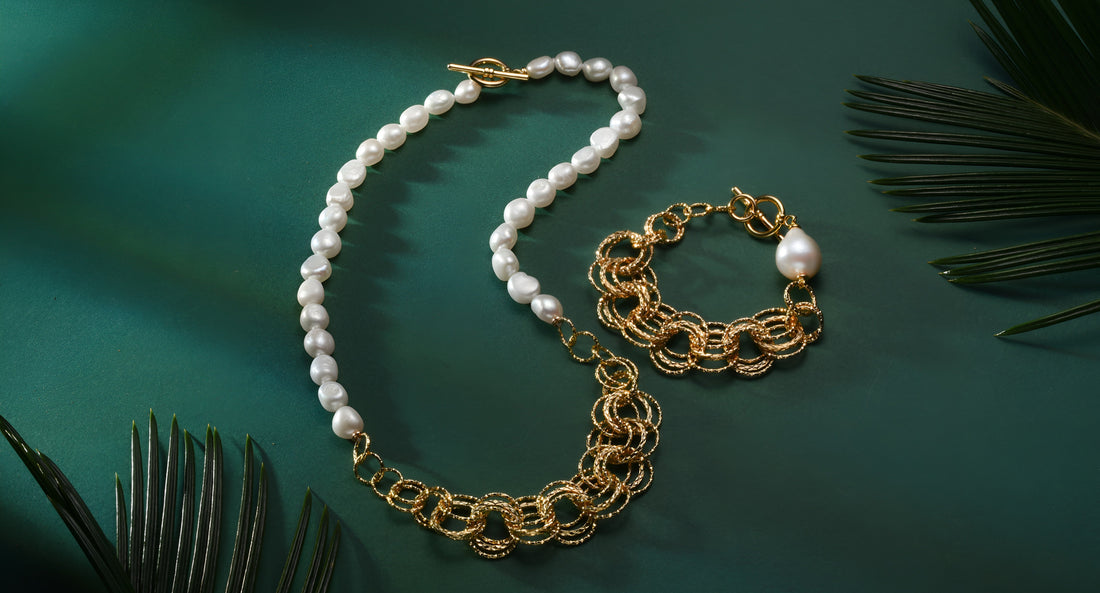 Timeless Pearl gold and freshwater jewelry set with long necklace and chain bracelet on green surface.