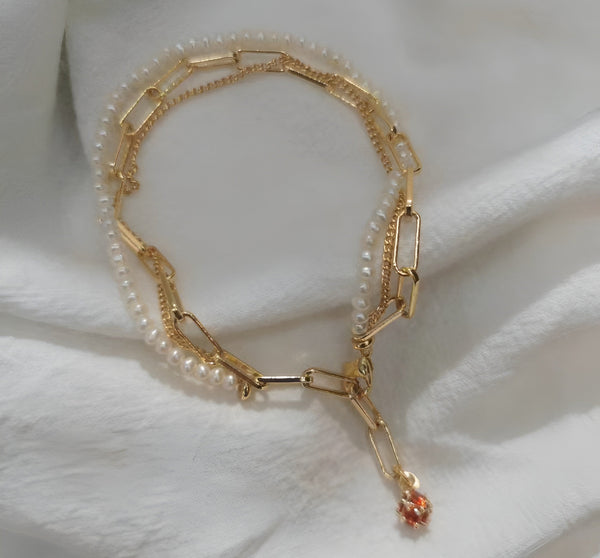 A Timeless Pearl necklace with golden strands and a bright reddish pearl laid out on a white sheet.