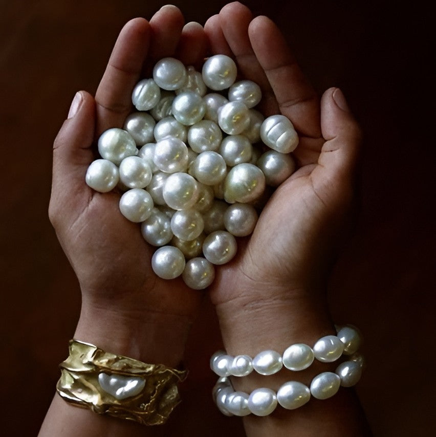 Hands wearing pearl bracelets while holding several white pearls.