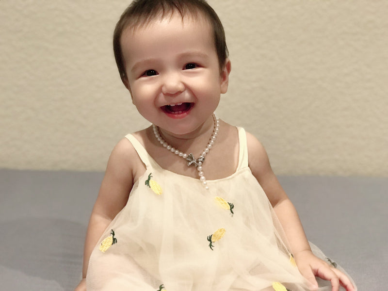 Smiling baby wearing a delicate pearl necklace for a sweet Timeless Pearl keepsake moment.