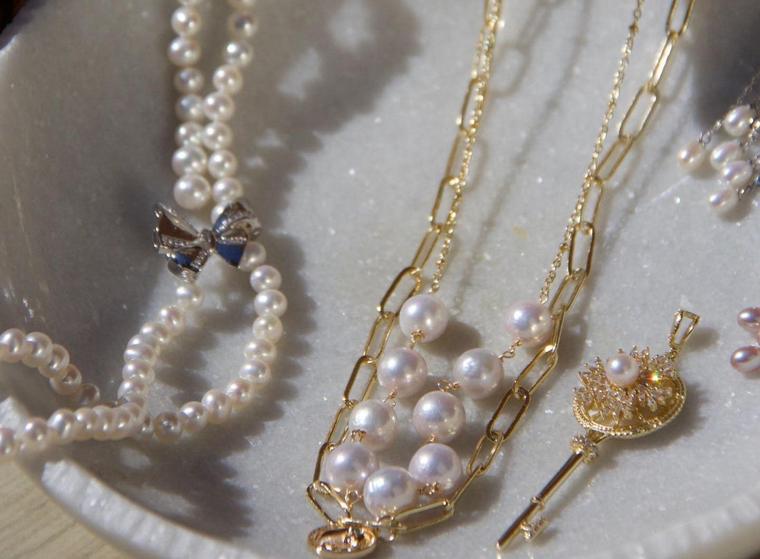 Timeless Pearl layered gold-chain necklaces and white pearl jewelry displayed in a ceramic dish under soft light.