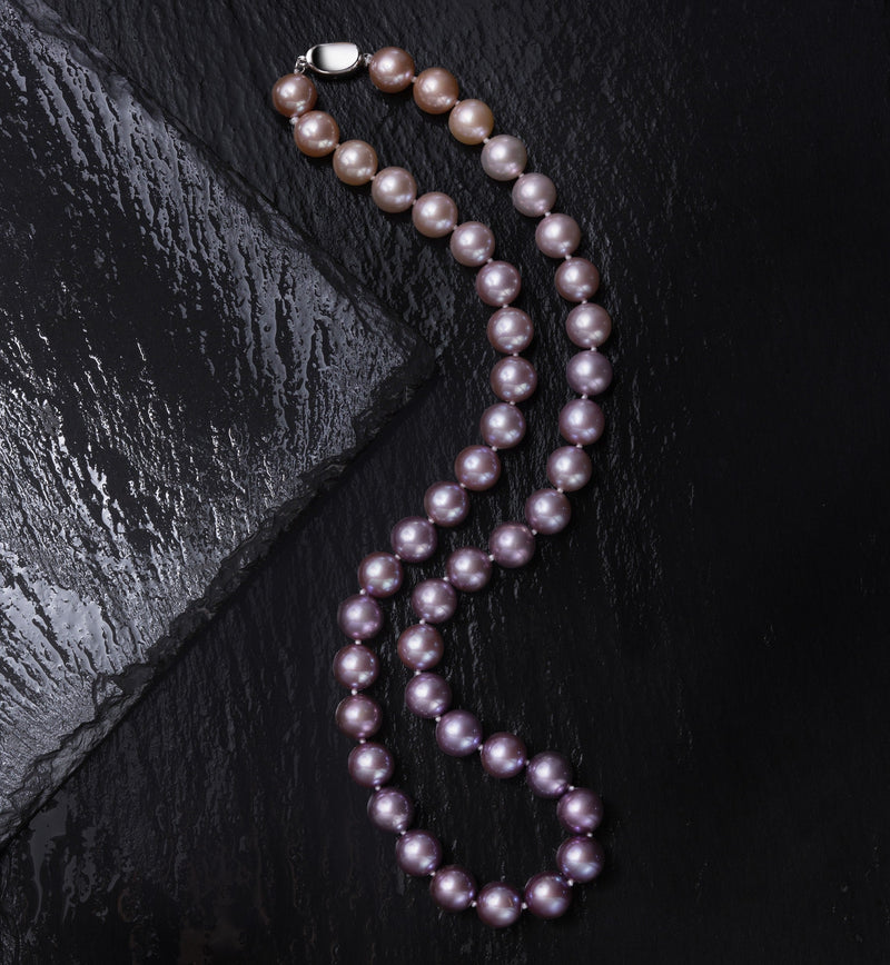 Timeless Pearl lavender pearl necklace with a silver clasp on a dark textured surface.