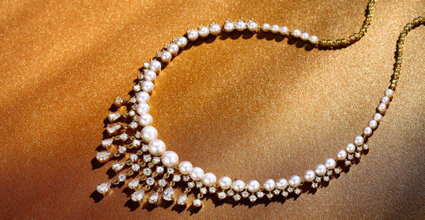Elegant Timeless Pearl and diamond necklace on a golden background, featuring round pearls and teardrop diamonds.