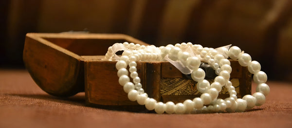 A close-up of Timeless Pearl necklaces spilling out of a small, wooden treasure box.