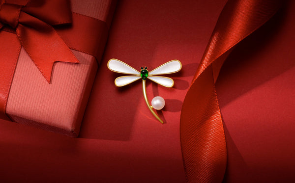 A Timeless Pearl piece surrounded by a tapered red ribbon and gift box.