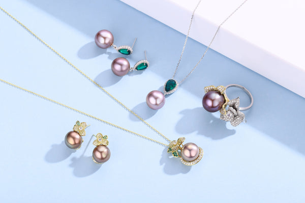 A flat lay of Timeless Pearl necklaces, earrings, and rings with mauve pearls and green gemstone accents.
