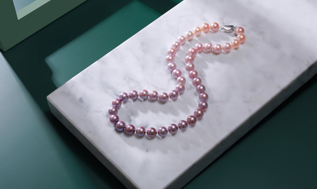 A gradient of pink pearls necklace arranged on a marble surface.