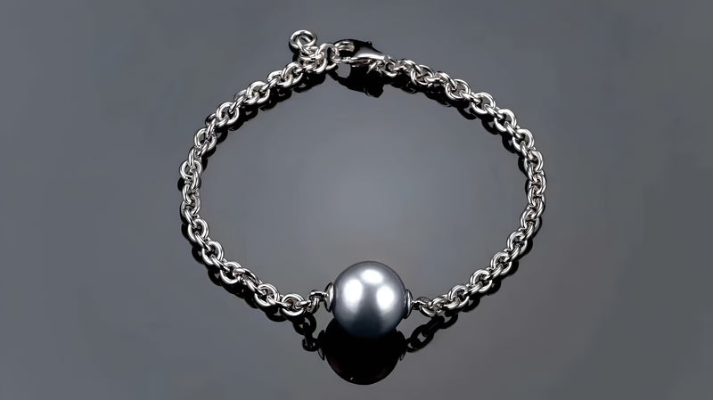 Timeless Pearl silver chain bracelet with a black pearl centerpiece on a gray surface.