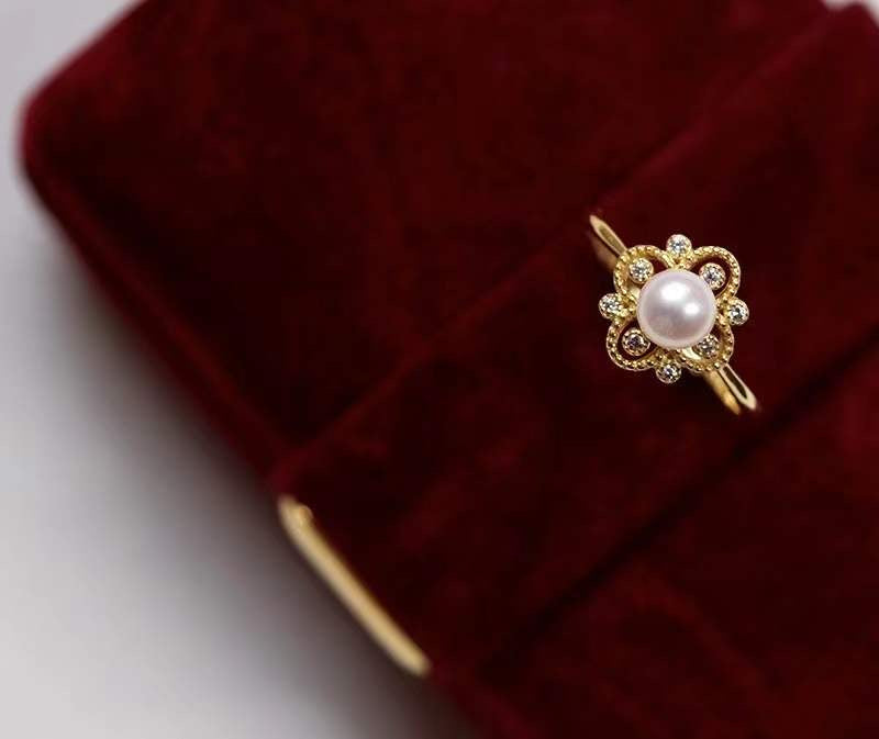 Timeless Pearl gold engagement ring with a central pearl and intricate floral detailing, displayed on red velvet.