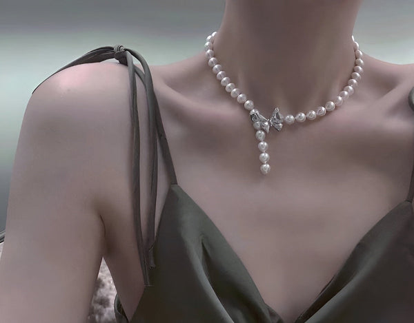 Woman wearing a Timeless Pearl necklace with white pearls and a bow-shaped center drop over a satin dress.