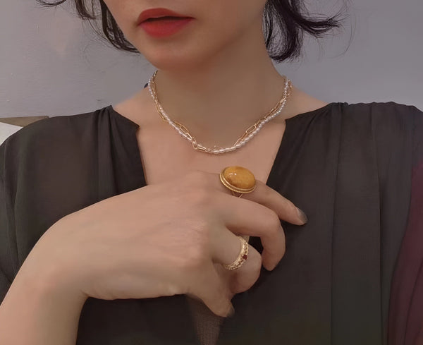  A woman wearing a Timeless Pearl necklace and bold gemstone rings, paired with a black top.