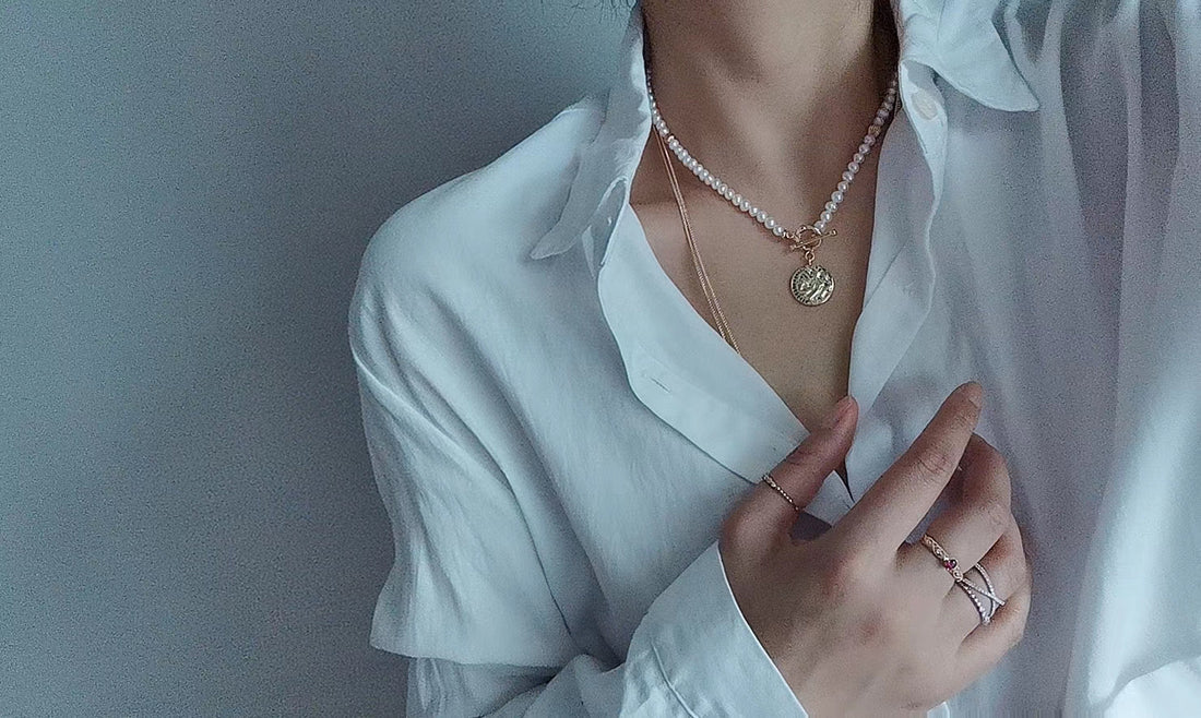 Timeless Pearl layered pearl necklace with a gold charm worn with a white button-down shirt.