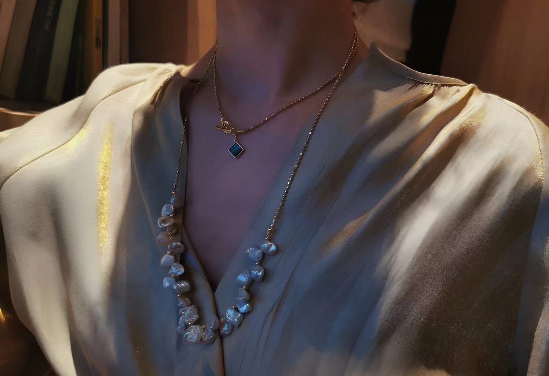  A woman wearing two-layered Timeless Pearl necklaces with gold strings and a green gemstone.