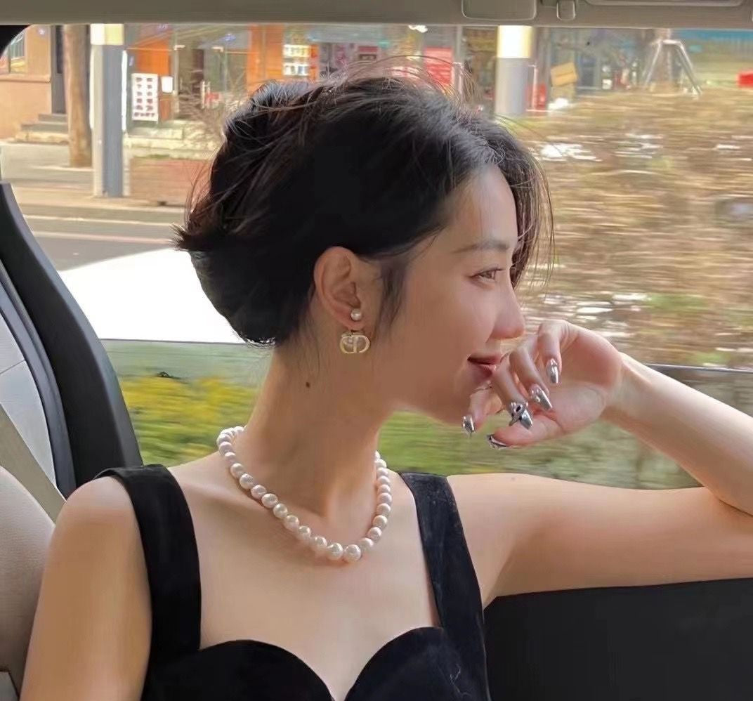 A woman wearing a pearl necklace and earrings from Timeless Pearl sits by a car window in a black dress.