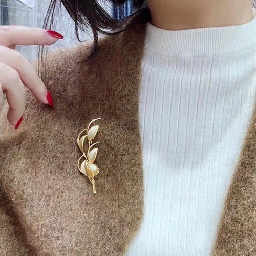 Timeless Pearls vintage-inspired gold brooch featuring a single golden pearl, worn on a brown coat with red nails.