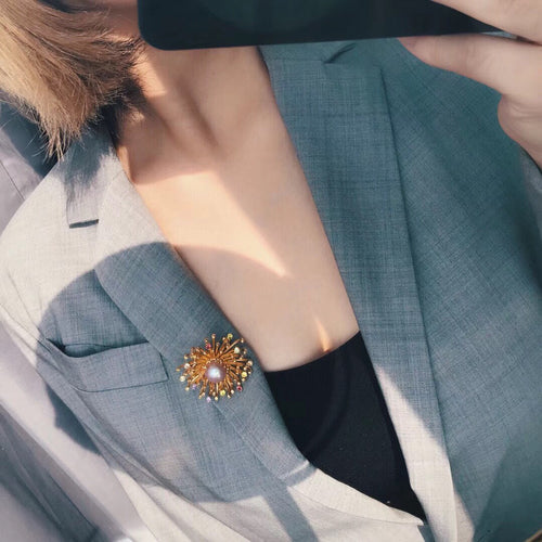 A close-up shot of a woman wearing a golden starburst brooch adorned with colorful stones, reflecting elegance and style by Timeless Pearls.