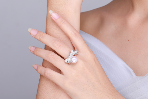 Hand wearing a pearl and diamond bow ring by Timeless Pearls