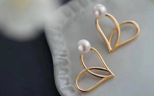 Gold heart-shaped earrings with freshwater pearls on a soft, elegant surface